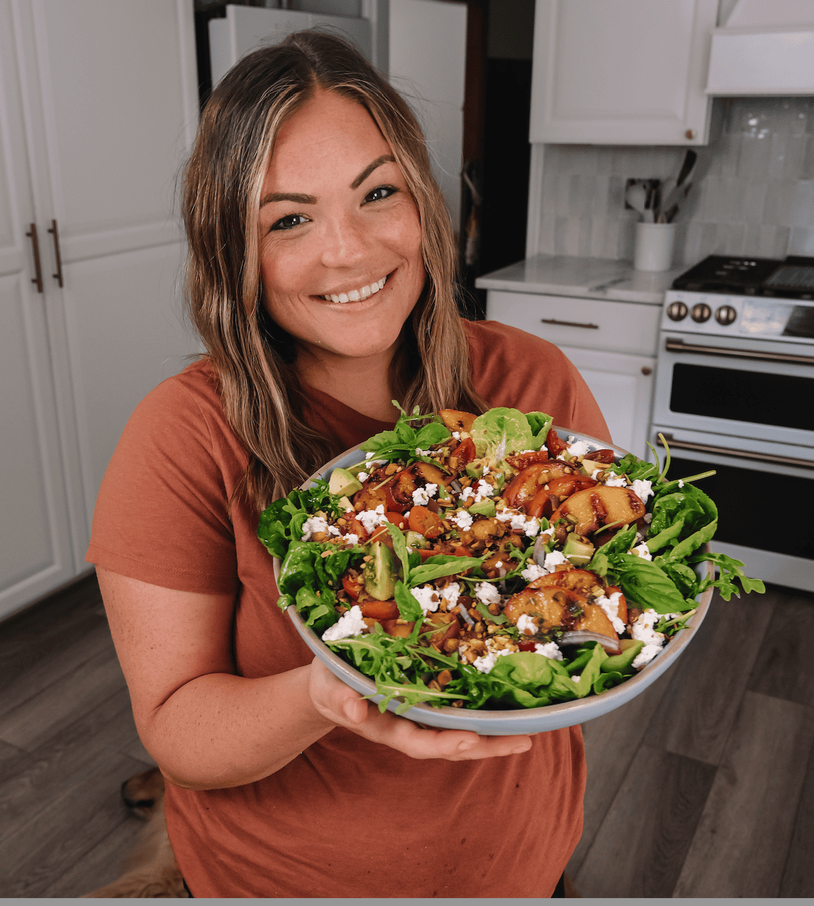 molly thompson holding a big bowl of grilled peach salad in the kitchen.